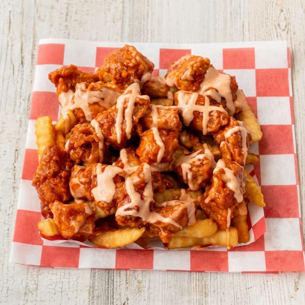 Crispy french fries topped with saucy boneless chicken wings and a creamy drizzle on checkered paper.
