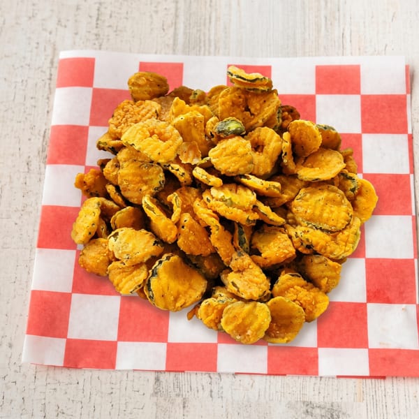A large pile of golden-brown fried pickles sits on a red and white checkered paper liner.