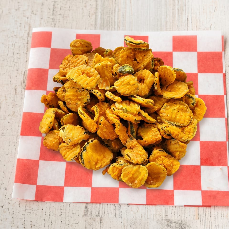 A large pile of golden-brown fried pickles sits on a red and white checkered paper liner.