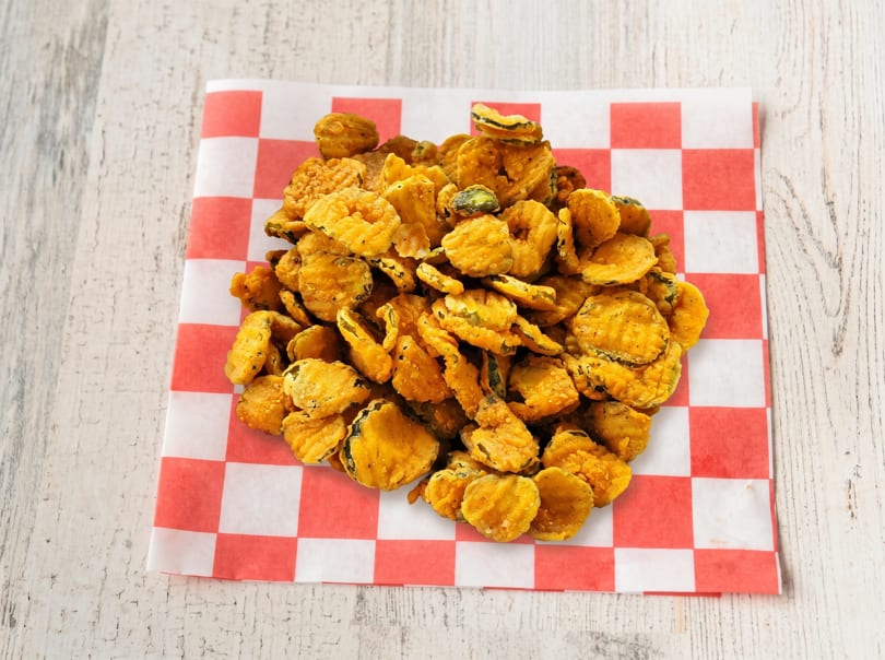A large pile of golden-brown fried pickles sits on a red and white checkered paper liner.