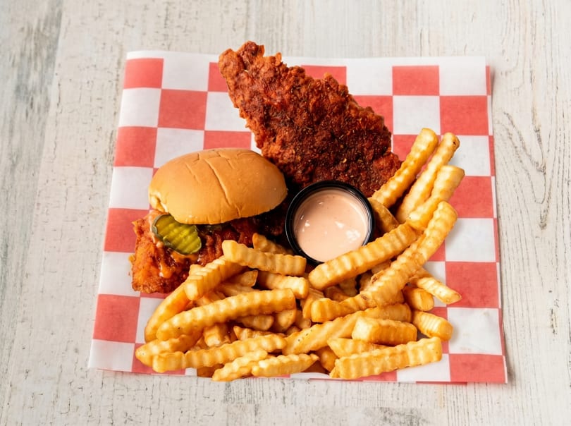 Spicy fried chicken sandwich with pickles, a large chicken tender, crinkle-cut fries, and dipping sauce.
