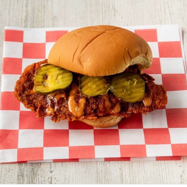Spicy fried chicken sandwich with pickles and sauce on a red and white checkered paper.