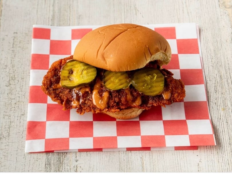 Spicy fried chicken sandwich with pickles and sauce on a red and white checkered paper.